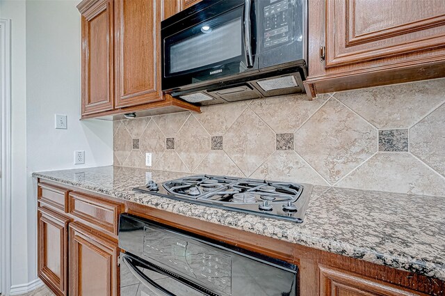 kitchen with black appliances, brown cabinetry, tasteful backsplash, and light stone countertops