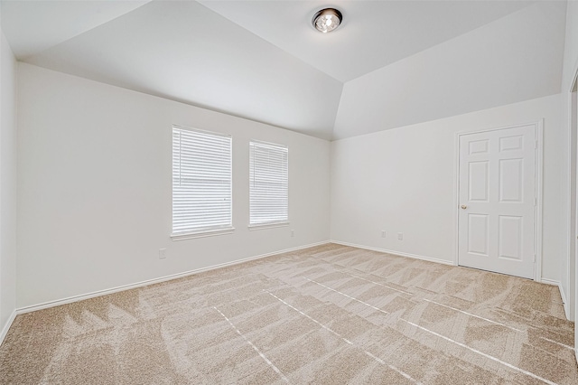 spare room with lofted ceiling, baseboards, and light carpet