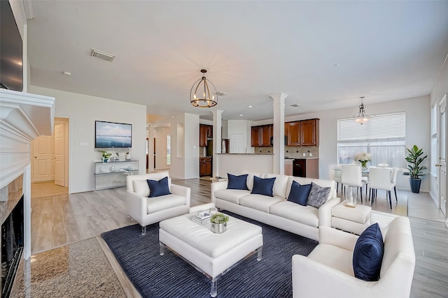 living room with visible vents, an inviting chandelier, a fireplace, light wood finished floors, and ornate columns