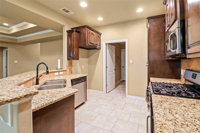 kitchen featuring appliances with stainless steel finishes, light stone counters, a raised ceiling, crown molding, and sink