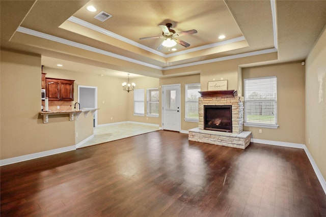 unfurnished living room with a fireplace, ceiling fan with notable chandelier, a tray ceiling, and dark wood-type flooring