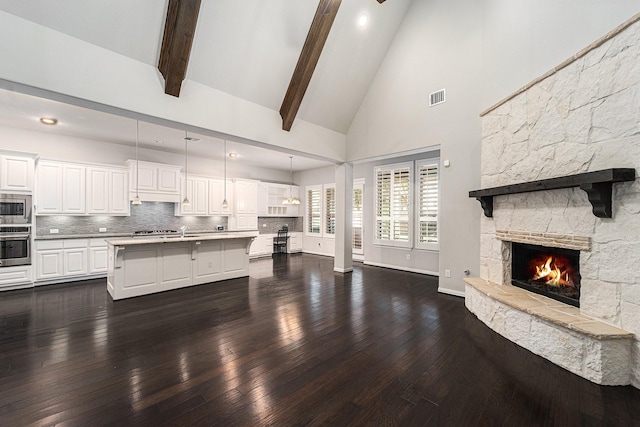 kitchen with pendant lighting, a kitchen island with sink, white cabinets, a stone fireplace, and stainless steel appliances