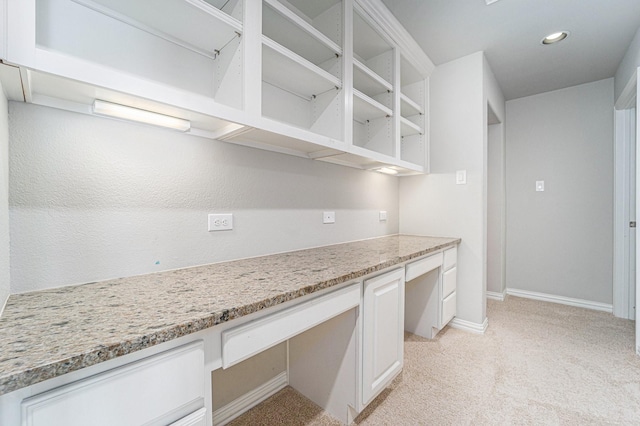 kitchen with white cabinets, light stone counters, built in desk, and light colored carpet