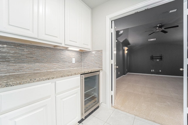 kitchen featuring light stone countertops, decorative backsplash, beverage cooler, light tile patterned floors, and white cabinetry