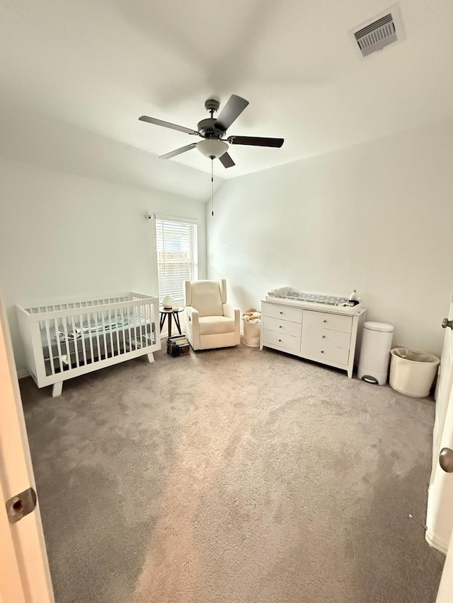 carpeted bedroom featuring ceiling fan and a crib