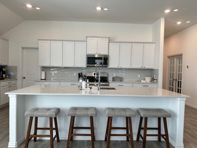 kitchen with a kitchen bar, appliances with stainless steel finishes, white cabinetry, and a large island with sink