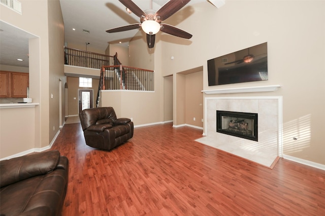 living room with hardwood / wood-style floors, ceiling fan, a towering ceiling, and a tiled fireplace