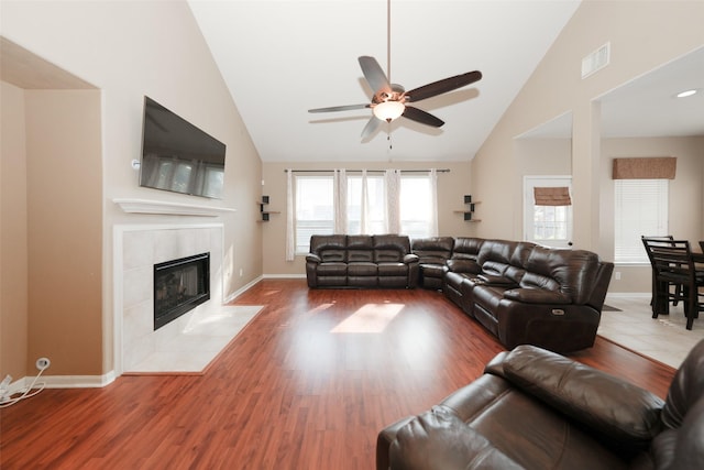 living room with a tiled fireplace, ceiling fan, vaulted ceiling, and hardwood / wood-style flooring