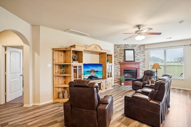 living room with a stone fireplace, ceiling fan, and hardwood / wood-style flooring