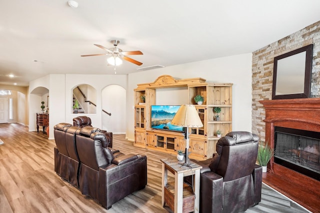 living room with hardwood / wood-style floors, a stone fireplace, and ceiling fan