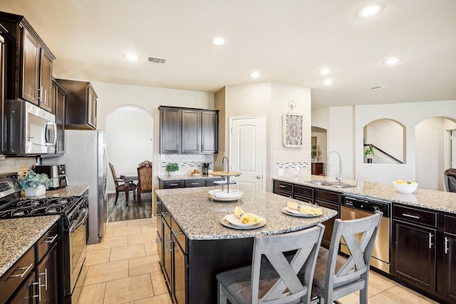 kitchen featuring appliances with stainless steel finishes, backsplash, sink, light tile patterned floors, and a center island