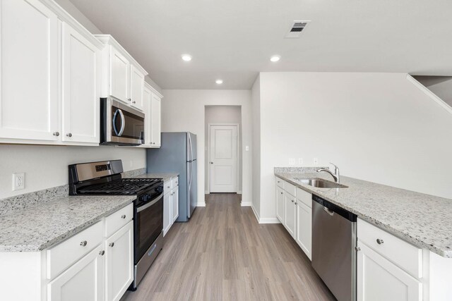 kitchen featuring white cabinetry, sink, light stone counters, light hardwood / wood-style flooring, and appliances with stainless steel finishes