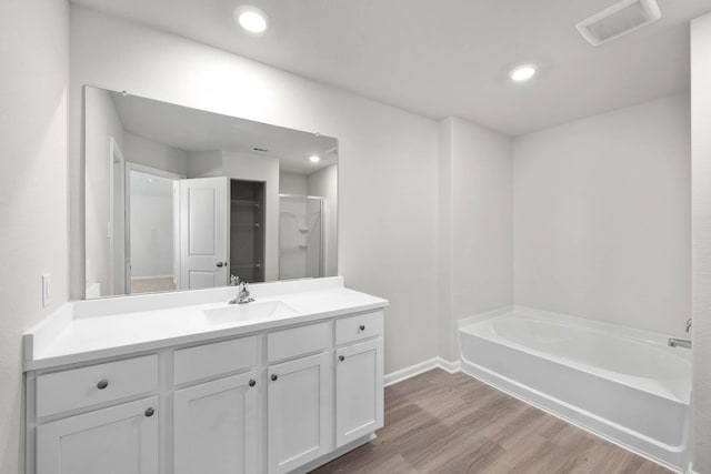 bathroom featuring plus walk in shower, vanity, and wood-type flooring