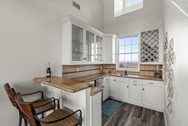 bar with backsplash, dark stone countertops, dark hardwood / wood-style flooring, and white cabinets