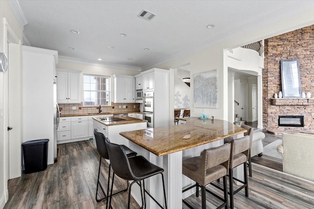 kitchen featuring dark hardwood / wood-style flooring, backsplash, electric stovetop, white cabinets, and a stone fireplace