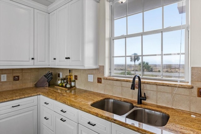 kitchen with white cabinets, backsplash, light stone counters, and sink