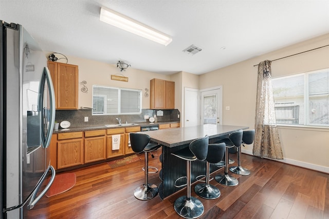 kitchen with a kitchen breakfast bar, stainless steel fridge, tasteful backsplash, a kitchen island, and dark hardwood / wood-style flooring