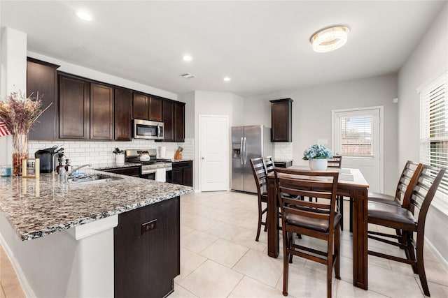 kitchen with light stone countertops, appliances with stainless steel finishes, decorative backsplash, and dark brown cabinets