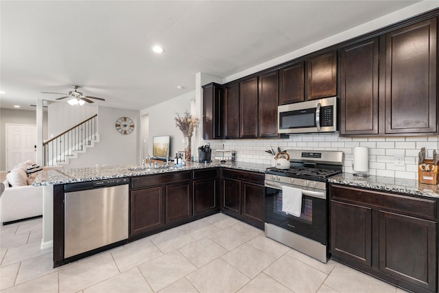 kitchen with kitchen peninsula, appliances with stainless steel finishes, decorative backsplash, light stone counters, and dark brown cabinetry