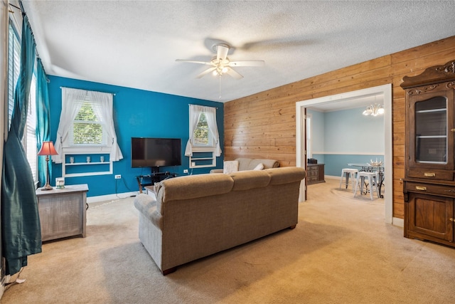 carpeted living room with ceiling fan with notable chandelier, a textured ceiling, and wood walls