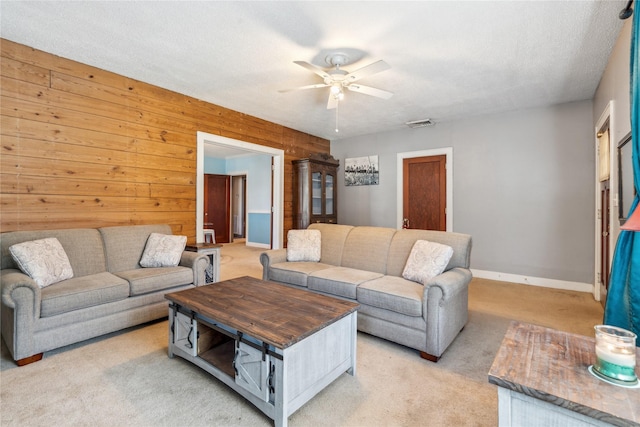 living room with a textured ceiling, ceiling fan, wood walls, and light carpet