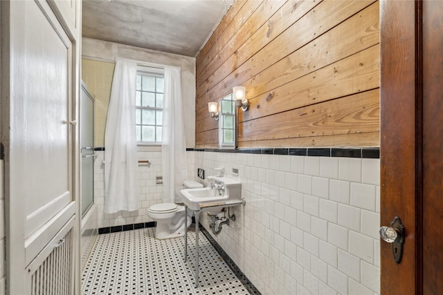 full bathroom featuring shower / bath combination with glass door, toilet, tile walls, and sink