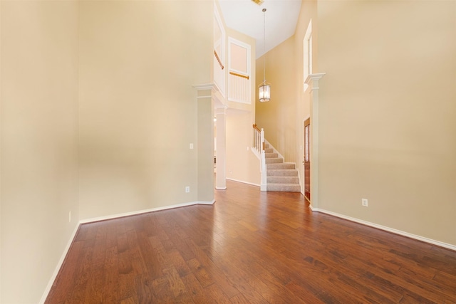 empty room with a notable chandelier, dark hardwood / wood-style floors, and a towering ceiling