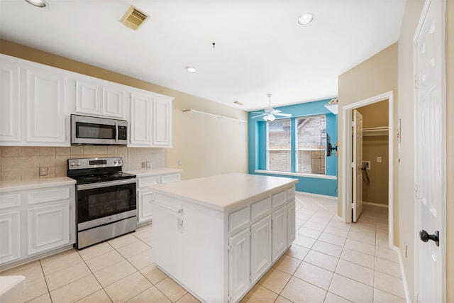 kitchen with white cabinets, stainless steel appliances, light tile patterned floors, and a kitchen island