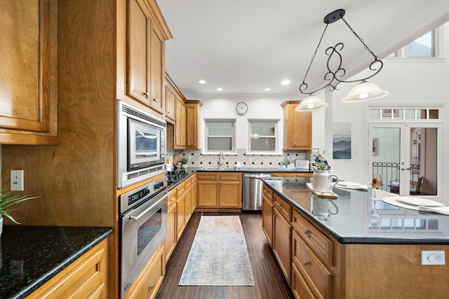 kitchen with stainless steel appliances, sink, decorative light fixtures, dark stone countertops, and dark hardwood / wood-style floors