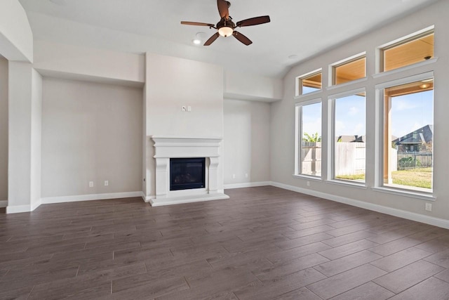 unfurnished living room with baseboards, dark wood-type flooring, and a glass covered fireplace