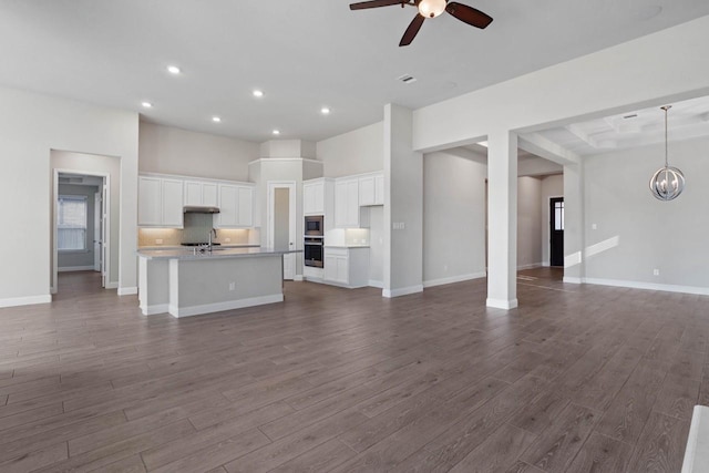 unfurnished living room with dark wood-style floors, recessed lighting, a sink, baseboards, and ceiling fan with notable chandelier