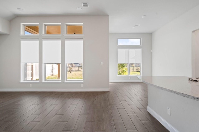 empty room with dark wood-type flooring, visible vents, and baseboards