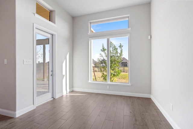 empty room with plenty of natural light, baseboards, and wood finished floors