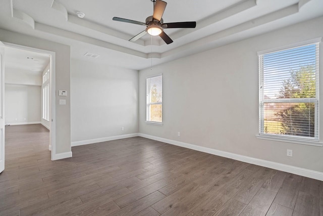 unfurnished room featuring dark wood-style flooring, a raised ceiling, and baseboards