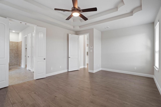 unfurnished room with ceiling fan, a tray ceiling, dark wood-type flooring, and baseboards