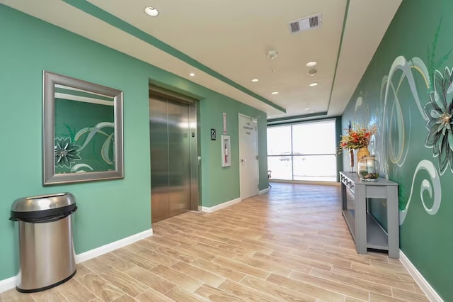 corridor with elevator, floor to ceiling windows, and light hardwood / wood-style floors