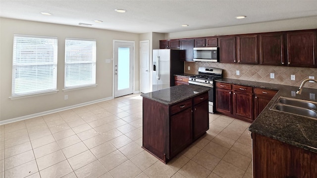 kitchen featuring sink, backsplash, dark stone countertops, a kitchen island, and appliances with stainless steel finishes