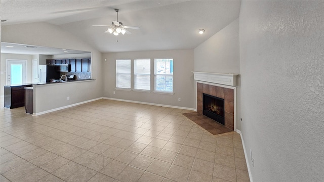 unfurnished living room featuring a tile fireplace, sink, vaulted ceiling, ceiling fan, and light tile patterned floors