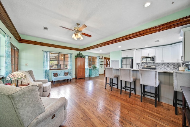 living room with a textured ceiling, hardwood / wood-style flooring, ceiling fan, and crown molding