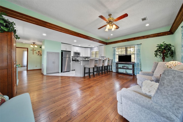 living room featuring ceiling fan, crown molding, light hardwood / wood-style floors, and a textured ceiling