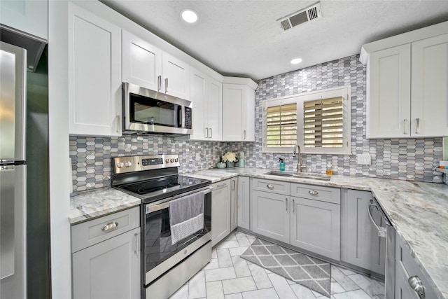 kitchen featuring backsplash, sink, light stone countertops, white cabinetry, and stainless steel appliances