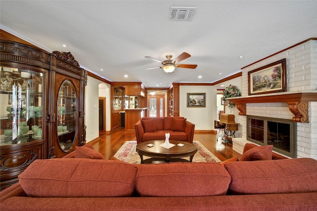 living room featuring ceiling fan, light wood-type flooring, a fireplace, and ornamental molding