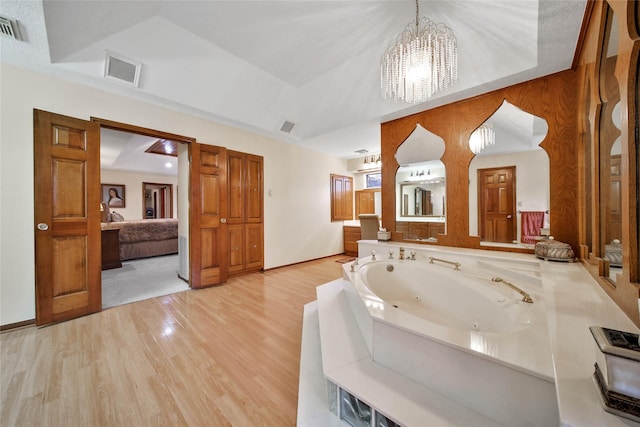 bathroom featuring wood-type flooring, a tray ceiling, a bathing tub, and a notable chandelier