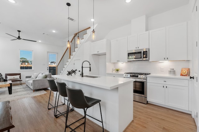 kitchen featuring appliances with stainless steel finishes, ceiling fan, sink, hanging light fixtures, and an island with sink