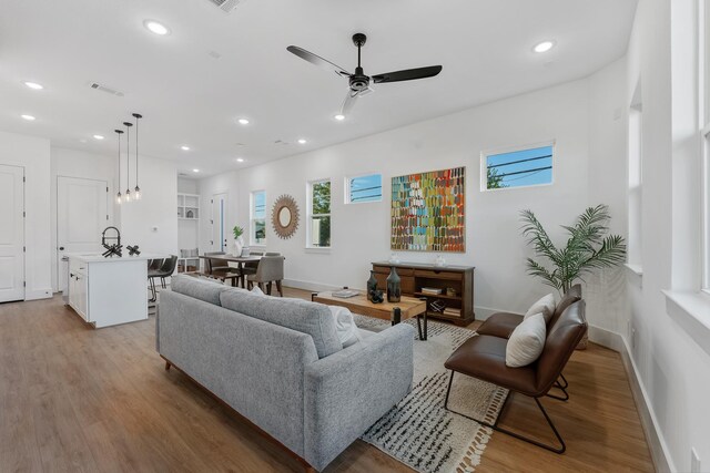 living room featuring ceiling fan, sink, and light wood-type flooring