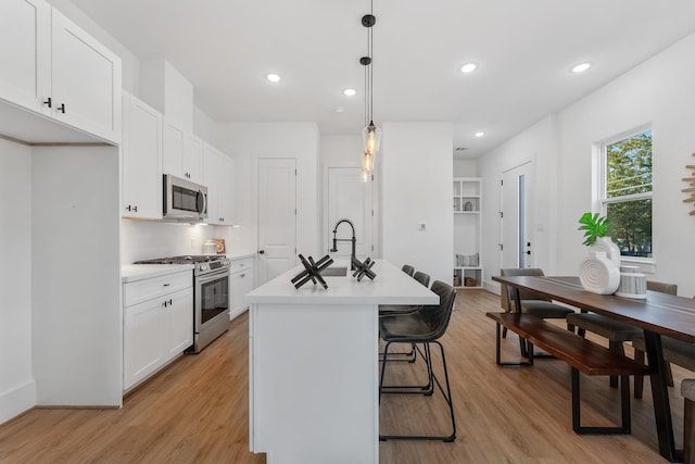 kitchen featuring white cabinets, hanging light fixtures, light hardwood / wood-style flooring, an island with sink, and stainless steel appliances