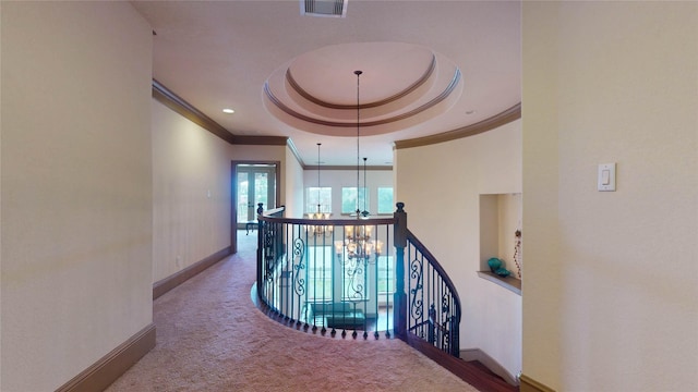 hall with a chandelier, carpet floors, ornamental molding, and a tray ceiling