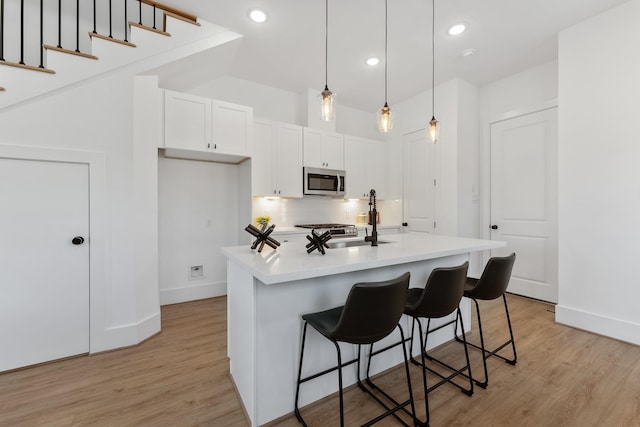 kitchen with hanging light fixtures, light hardwood / wood-style flooring, an island with sink, appliances with stainless steel finishes, and white cabinetry