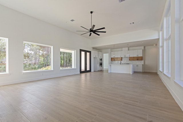 unfurnished living room featuring plenty of natural light, ceiling fan, light hardwood / wood-style floors, and sink