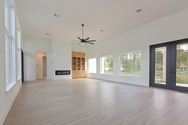 unfurnished living room featuring ceiling fan, french doors, a high ceiling, and plenty of natural light